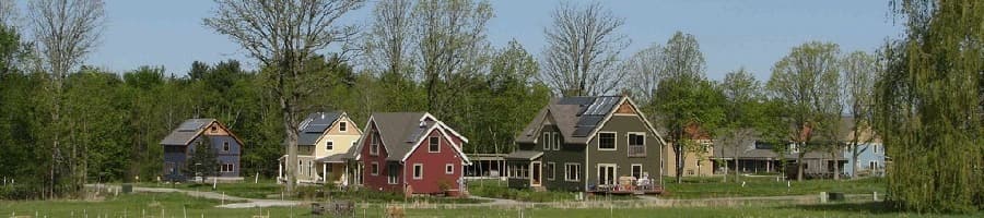 CVC's homes — red, green, blue, and yellow farmhouse-style houses with solar panels — across a green meadow in spring