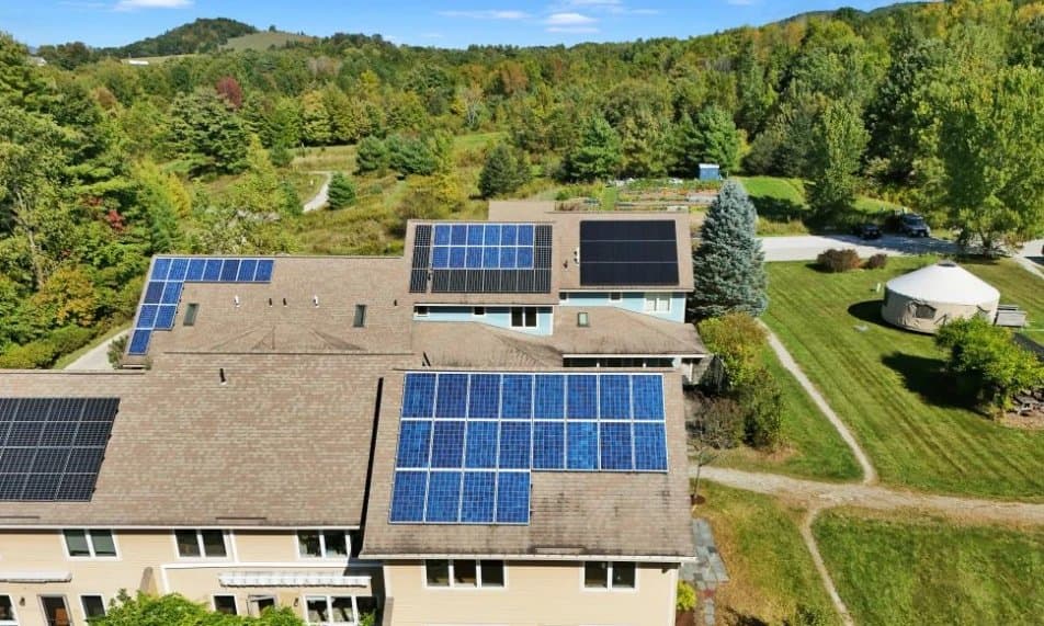 Solar panels covering the roofs of CVC's homes, with the green, the yurt, and wooded hills beyond